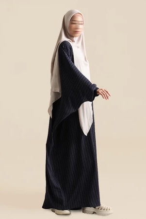 Person wearing abaya by Nehhat Modest with a white hijab on a beige background