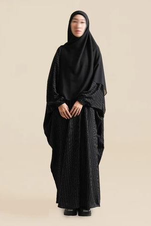 Person wearing a black abaya by Nehhat Modest on a beige background