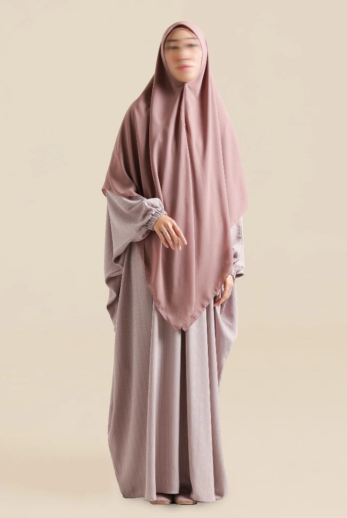 Woman wearing a dusty rose abaya by Nehhat Modest with a matching hijab on a beige background