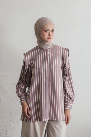 Woman wearing a striped dusty and white shirt by Maima and hijab against a white wall.