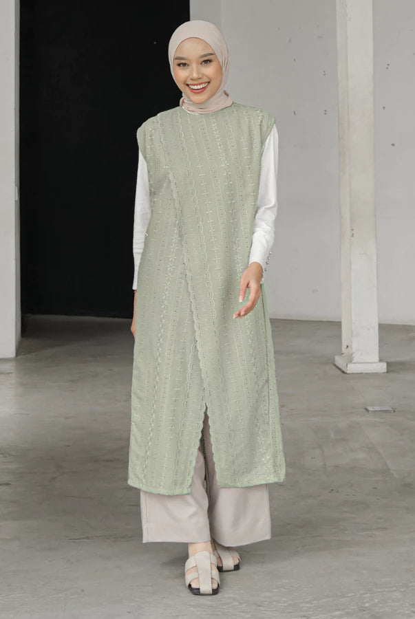 Woman wearing a light green sleeveless long vest by Mistyvori and beige pants in an indoor setting