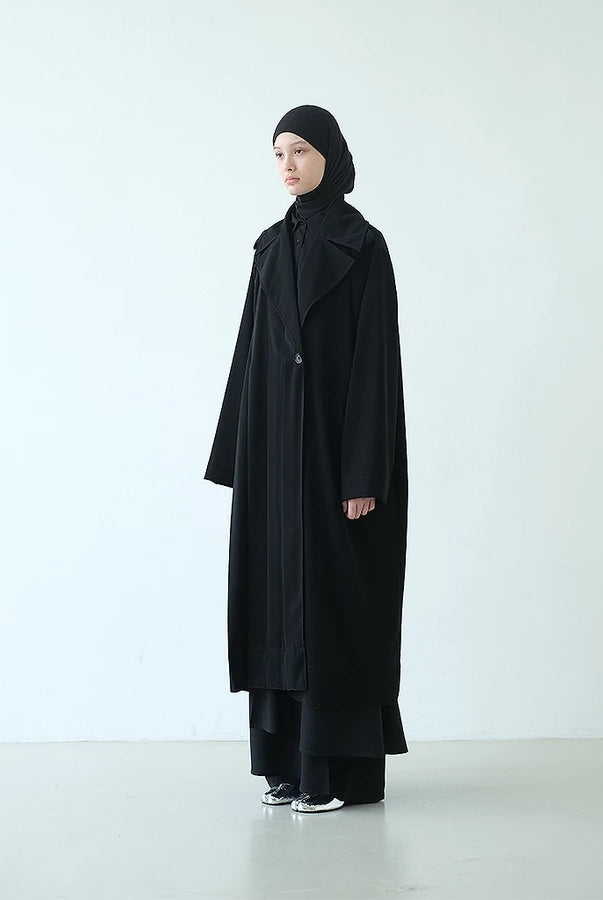 Person wearing a long black coat by Rashawl and headscarf on a white background