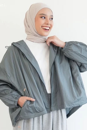 Woman wearing a gray jacket by Mistyvori over a white outfit with a beige hijab on a light background