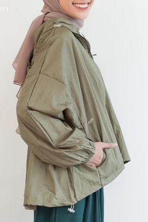 Person wearing a green jacket by Mistyvori with a pink headscarf on a plain background