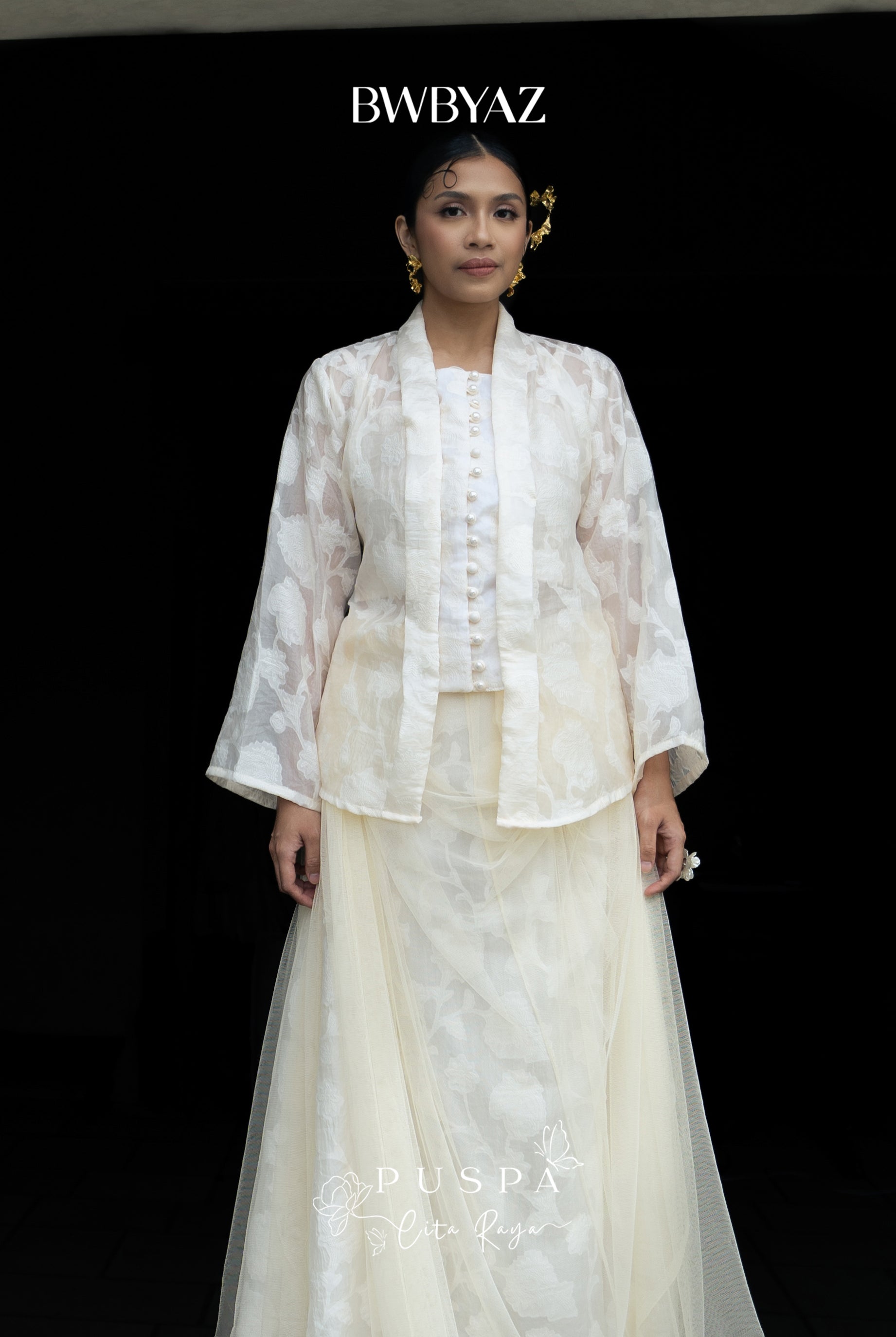 Woman wearing a white kebaya with lace details on a black background and 'BWBYAZ' branding.