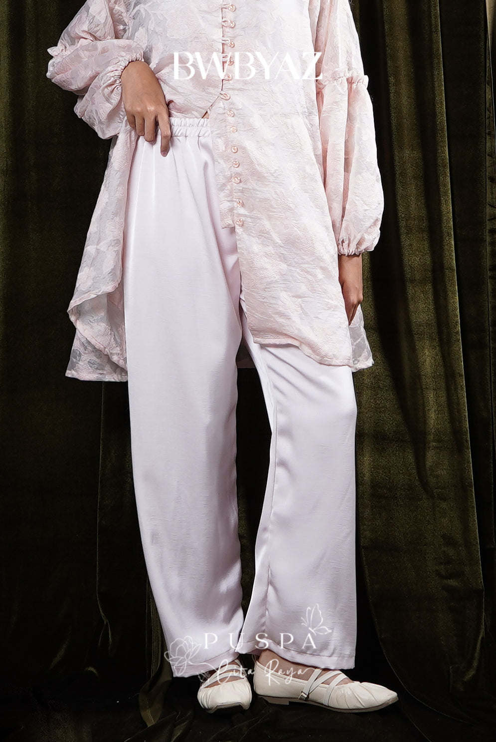 Person wearing a light pink trousers by BWBYAZ against a dark curtain background.