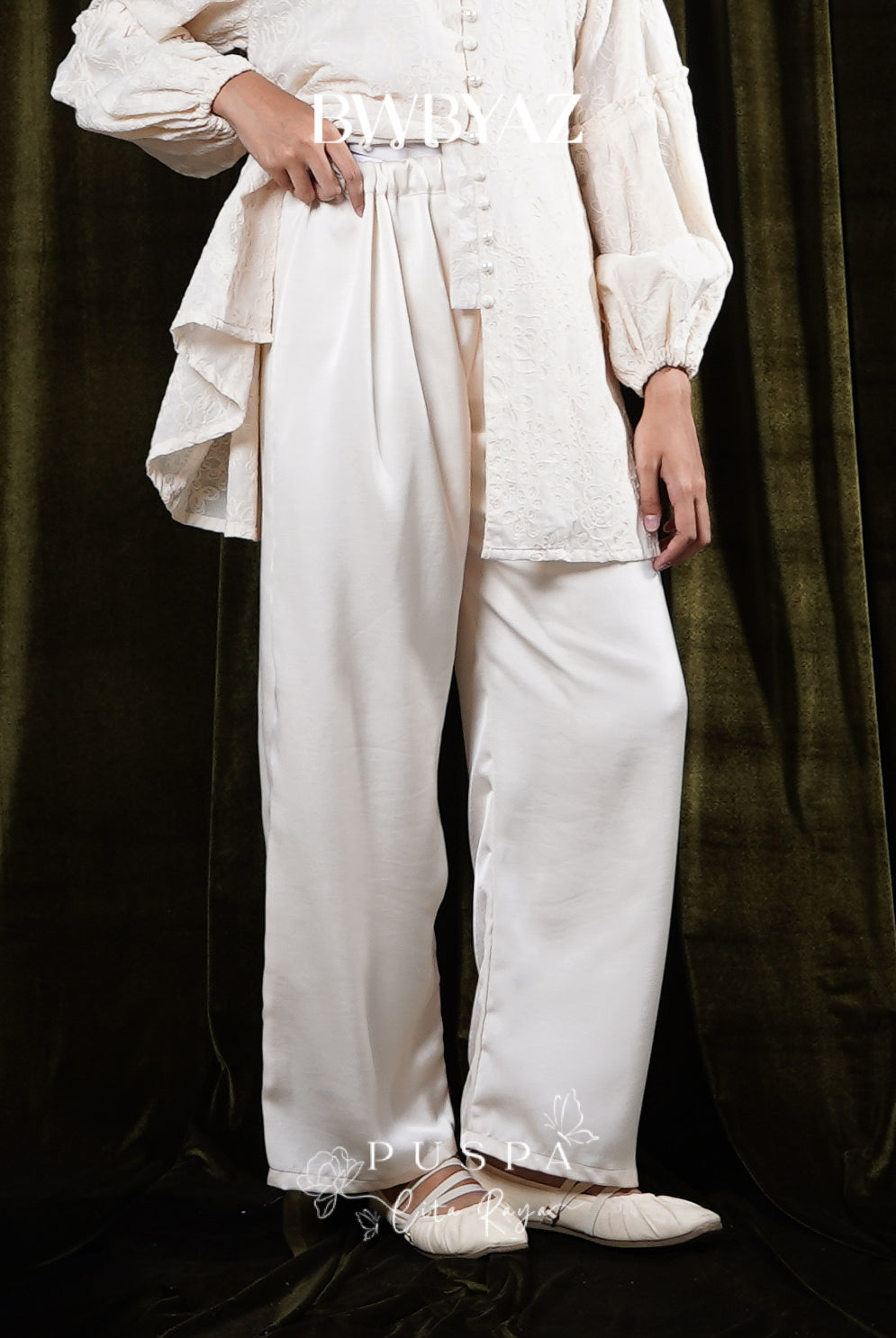 Person wearing a white trousers by BWBYAZ against a dark curtain background
