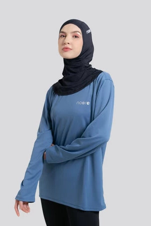 Woman wearing a blue long-sleeve top by Noore and black hijab on a gray background