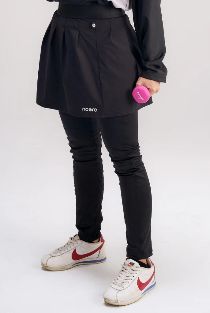 A person wearing a black activewear skirt with the brand name 'noore' visible on the front, paired with leggings and sneakers.