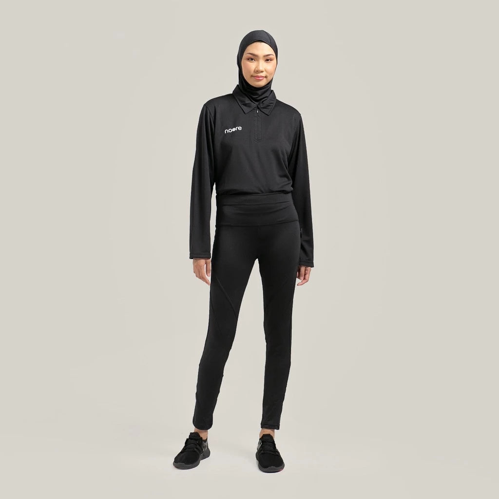 A person wearing a black legging by Noore and a matching black top, standing against a plain background.