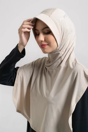 Woman wearing a beige sport hijab by Noore against a plain background.