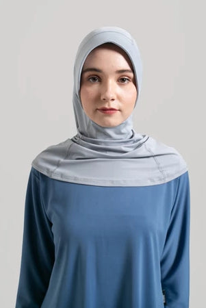 Woman wearing a light gray hijab and blue top from Noore on a plain background