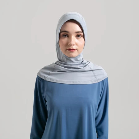 Woman wearing a light gray hijab and blue top from Noore on a plain background