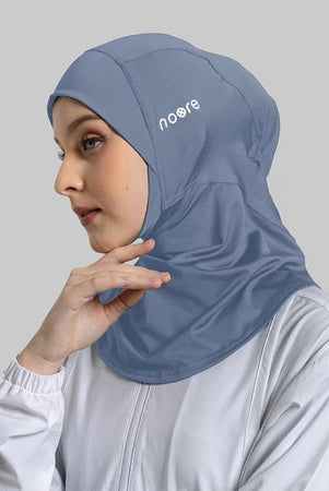 Woman wearing a blue sport hijab with 'Noore' branding on a gray background