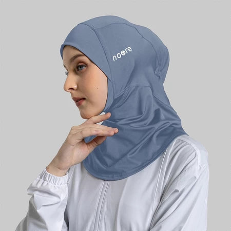 Woman wearing a blue sport hijab with 'Noore' branding on a gray background