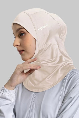 Woman wearing a beige sport hijab with a Noore logo on a gray background