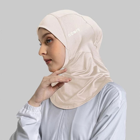 Woman wearing a beige sport hijab with a Noore logo on a gray background