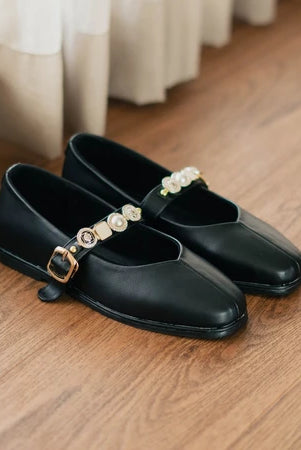 Black flat shoes with pearl embellishments by Dianable on a wooden floor