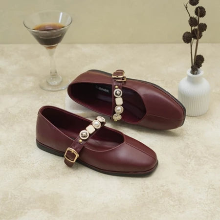 Pair of maroon flat shoes with decorative buckles by Dianable on a beige surface.