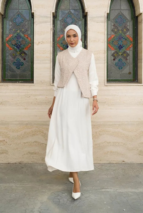 Woman in a white dress by Tunique with a beige vest standing in front of a building with stained glass windows.