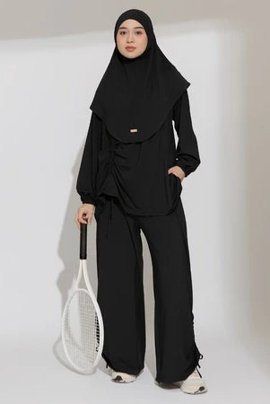 Person wearing a black hijab activewear set by Lozy Hijab holding a tennis racket on a plain background