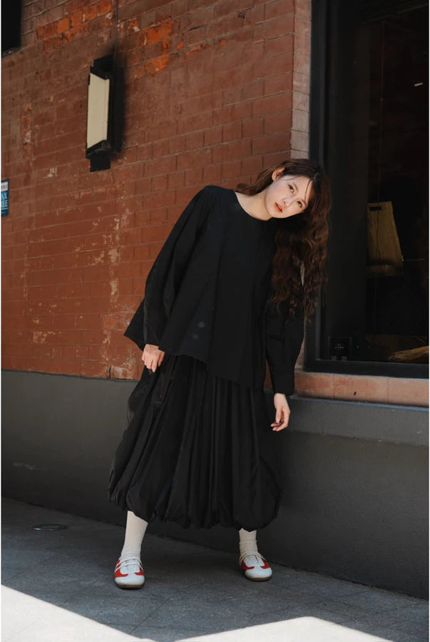 Woman wearing a black top and balloon pleated skirt by Yestoday standing against a brick wall.