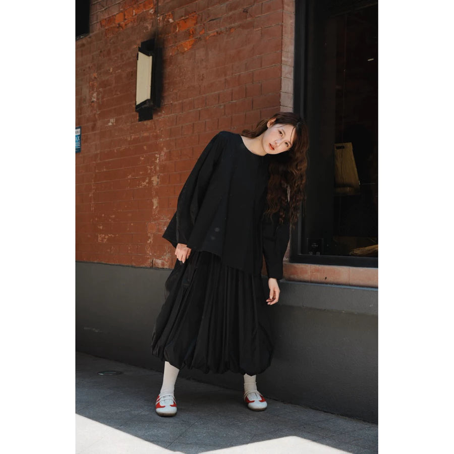 Woman wearing a black top and balloon pleated skirt by Yestoday standing against a brick wall.