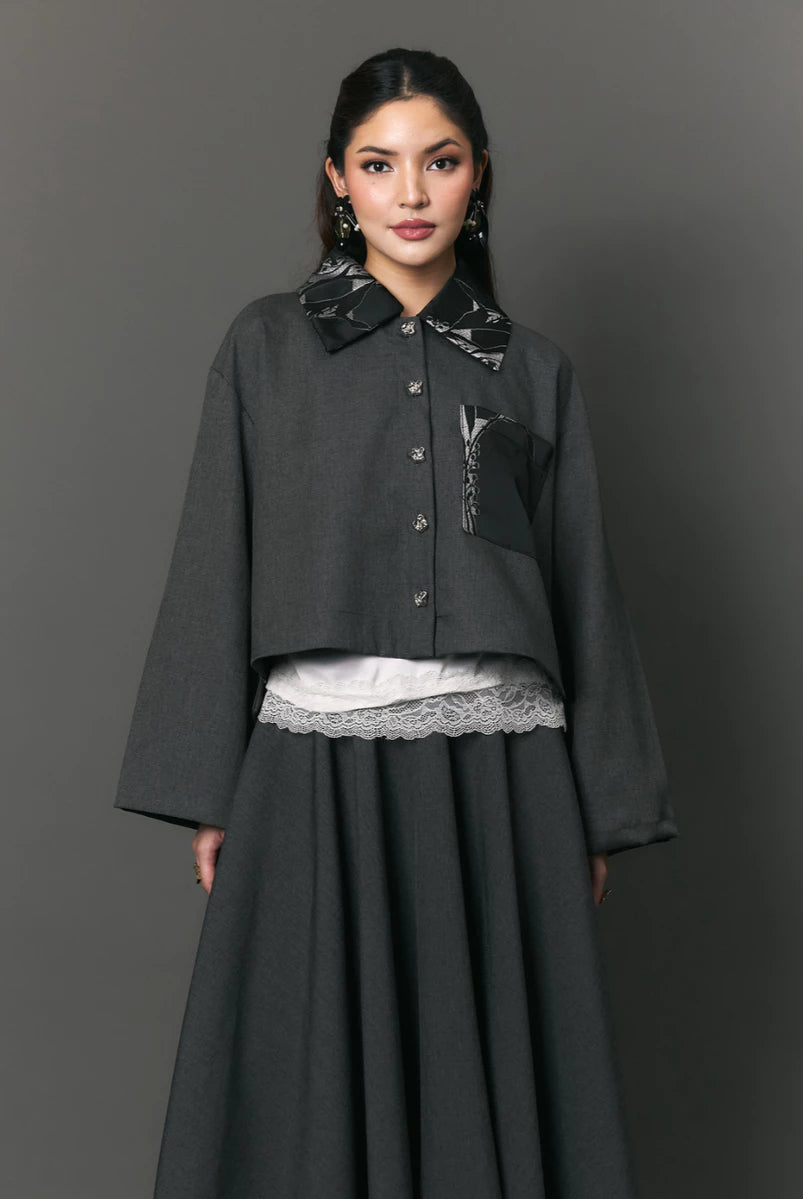 Woman wearing a dark gray outer with patterned collar and pockets by Studio Tui on a gray background