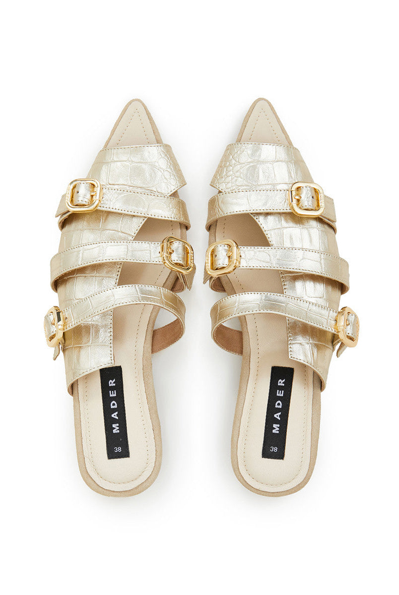 A pair of gold open toe mules with crocodile pattern leather upper and buckle details. The brand's signature outsole is visible.