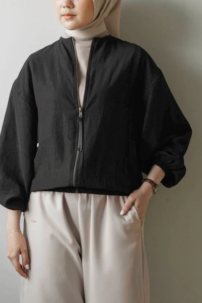 Person wearing a black jacket by Mistyvori and light-colored pants against a plain background