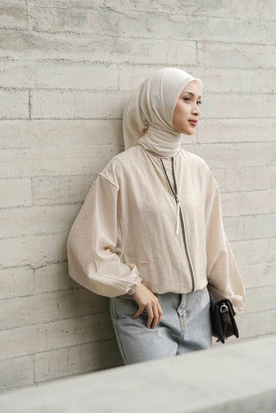 Woman wearing a beige hijab and cream jacket by Mistyvori against a textured wall.