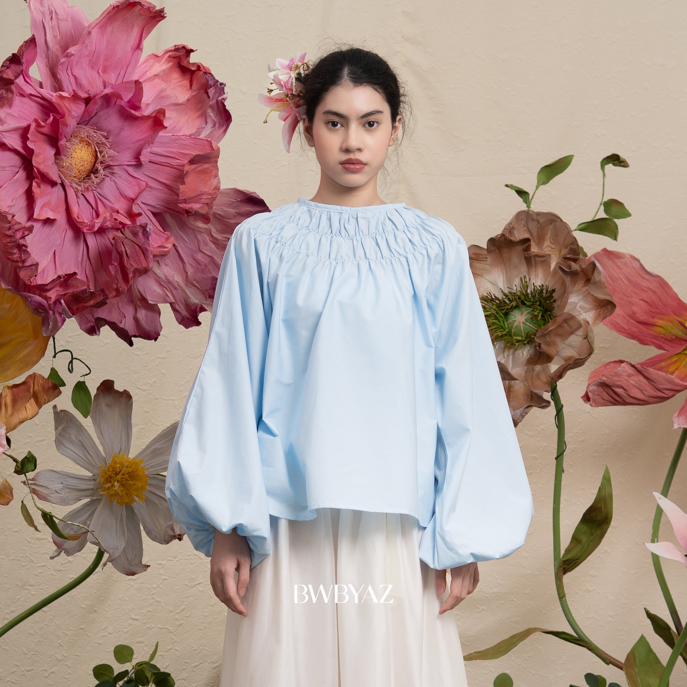 Woman wearing a light blue blouse by BWBYAZ with floral background