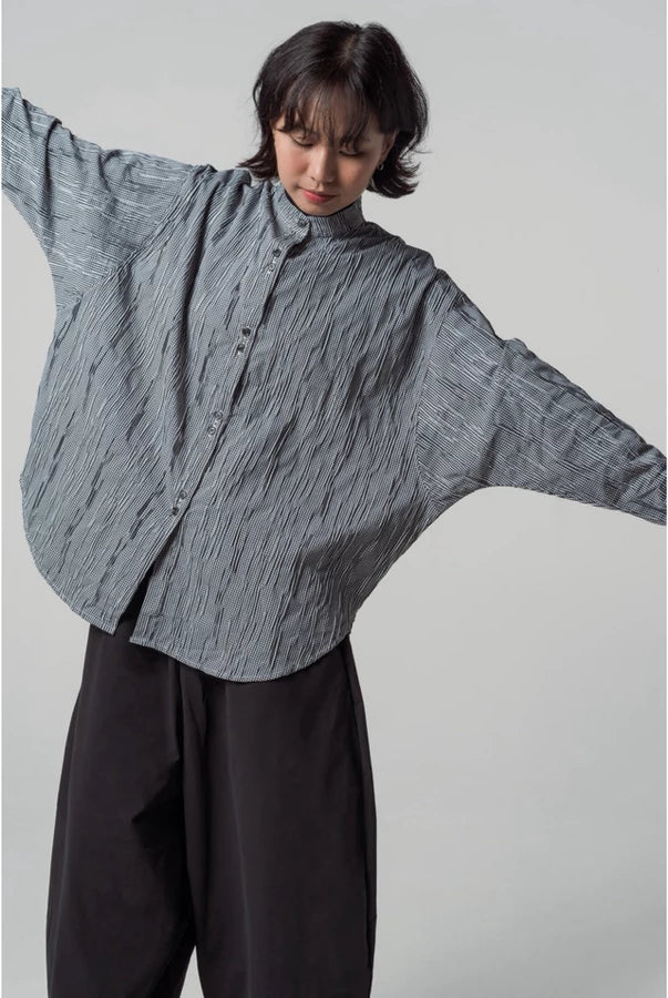 Person wearing a loose-fitting, long-sleeve, black and white shirt by Yestoday with a white background
