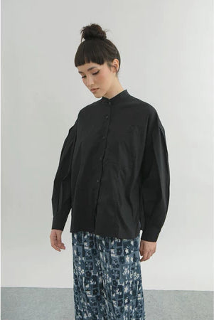 Person wearing a black shirt by Yestoday and patterned pants against a plain background