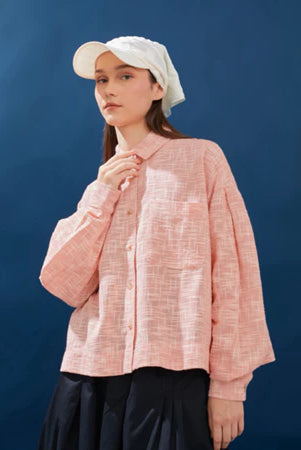 Person wearing a white with pink-textured shirt and white cap against a blue background