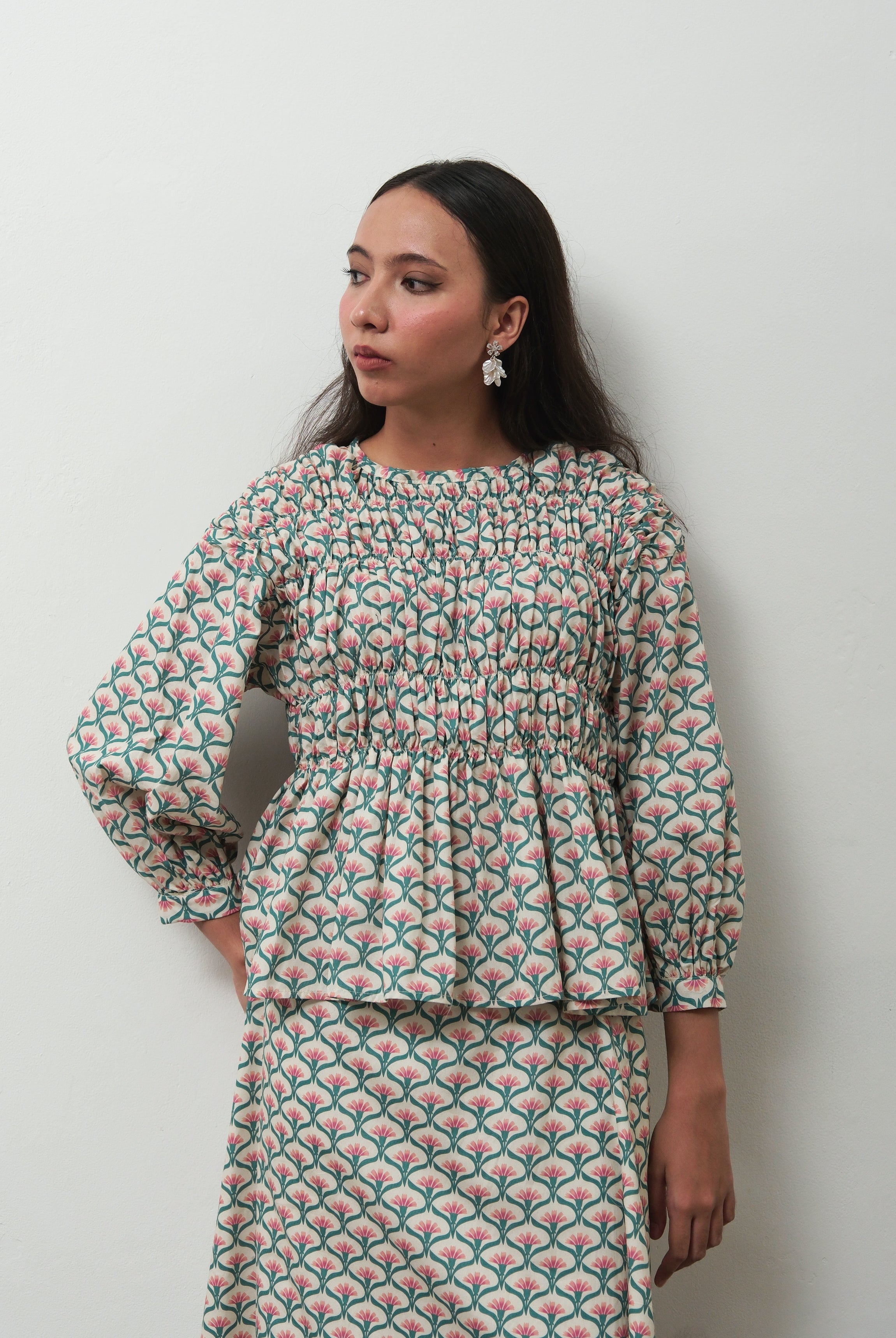 A woman wearing a matching two-piece set by BWBYAZ with a green, pink, and white scallop pattern, standing against a plain light gray wall.