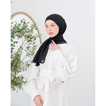 Woman wearing a black pashmina hijab and white outfit with a plant in the background