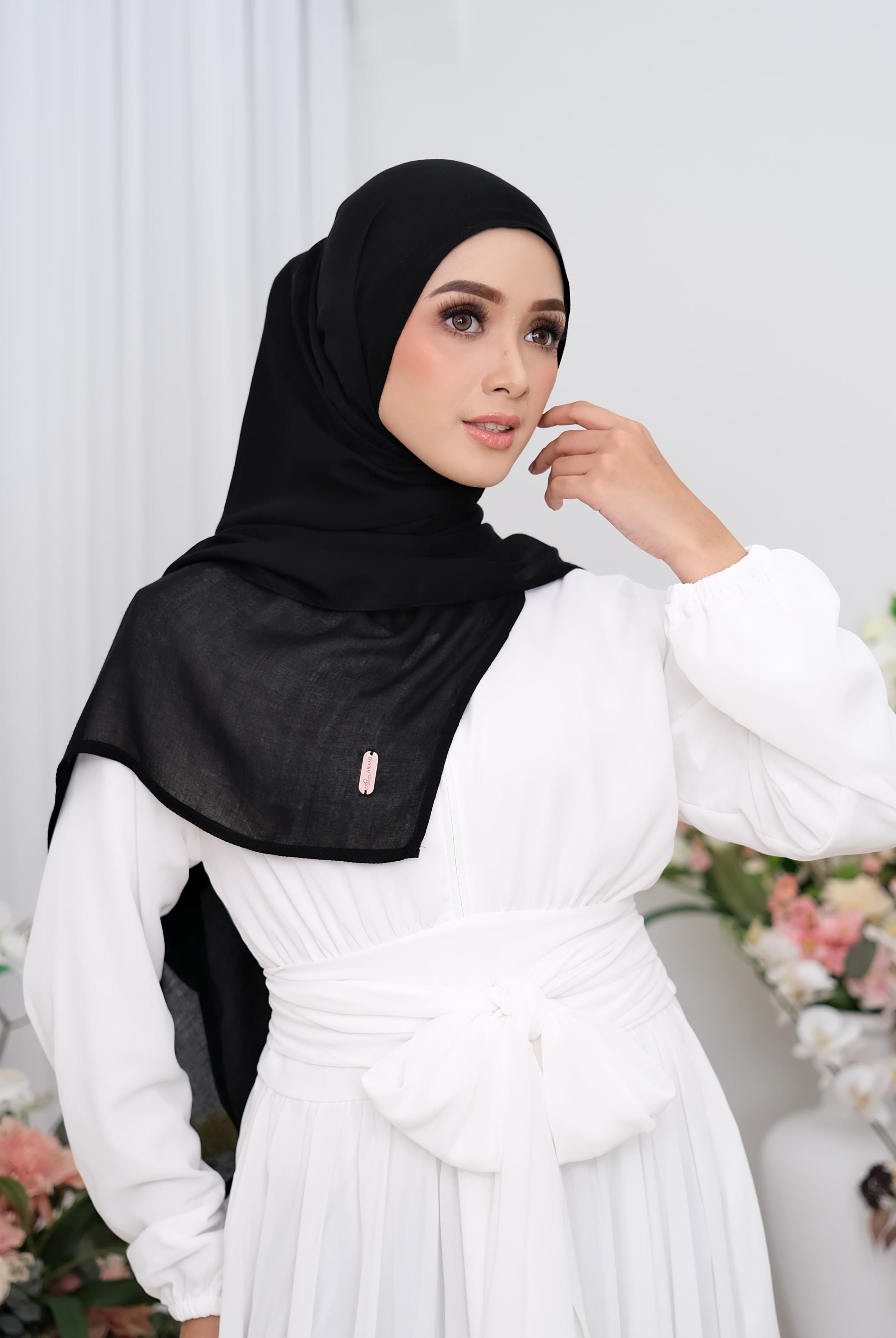 Woman wearing a black hijab pashmina viscose and white dress in a floral setting