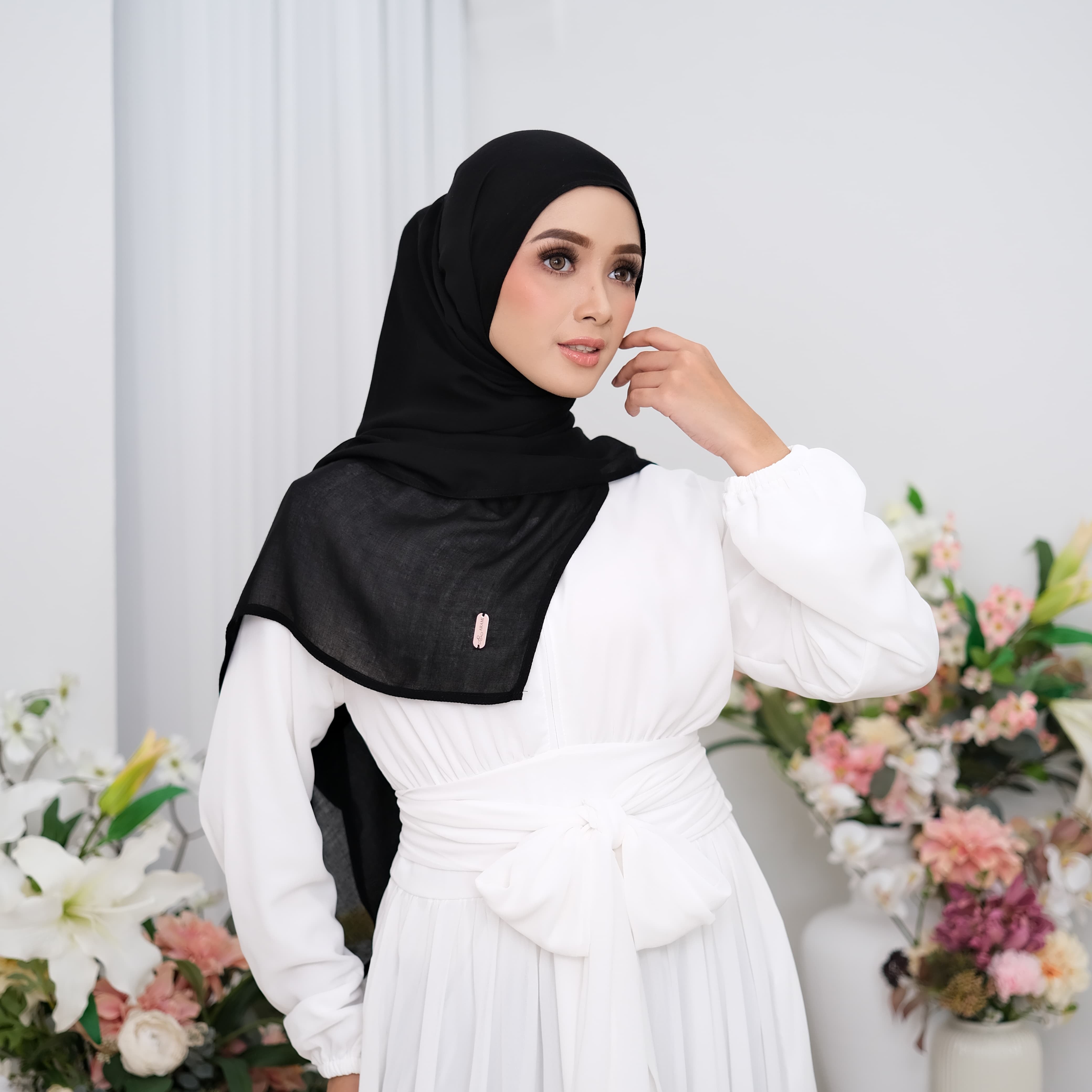 Woman wearing a black hijab pashmina viscose and white dress in a floral setting