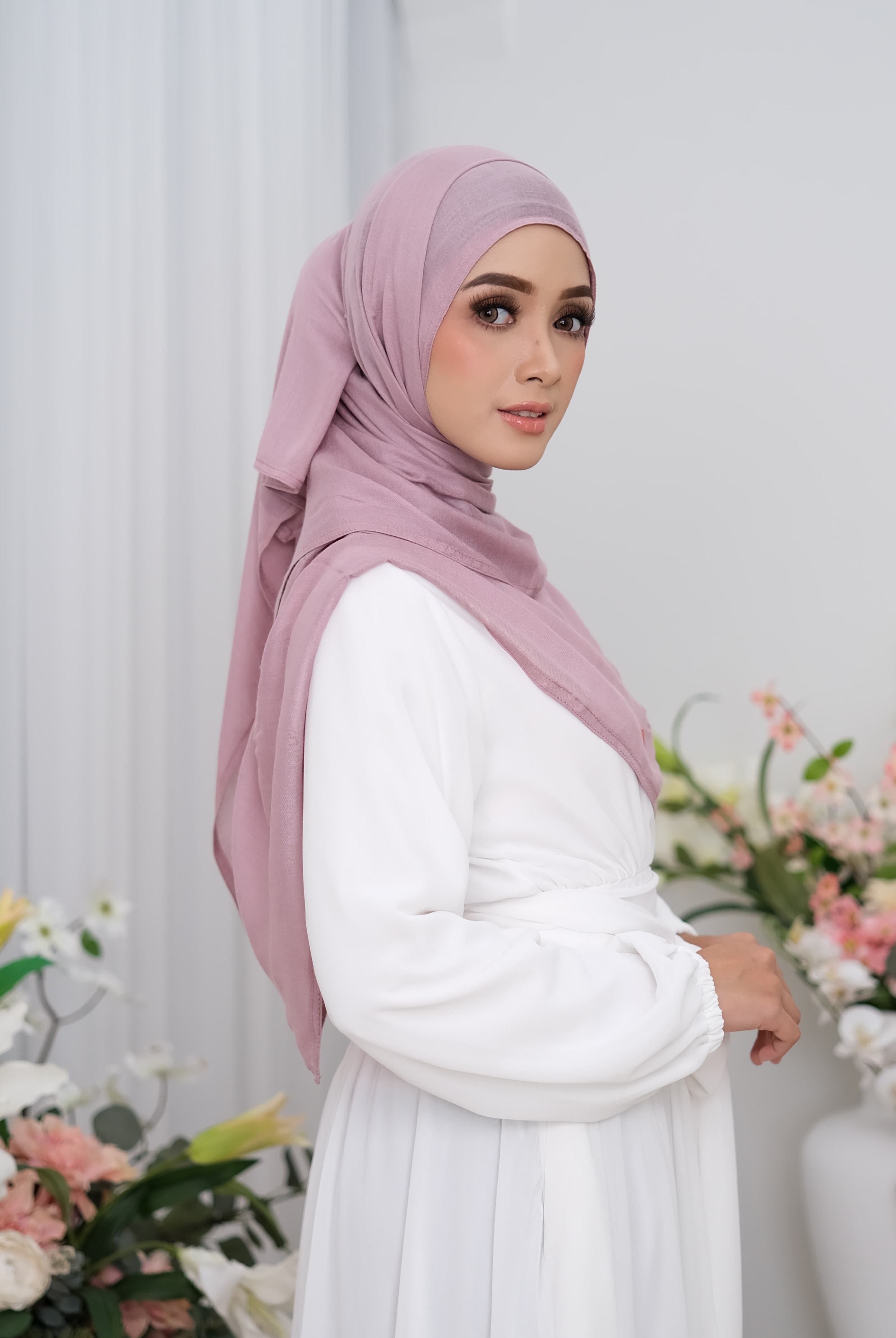 Woman wearing a pink hijab pashmina viscose and white outfit with floral decorations in the background
