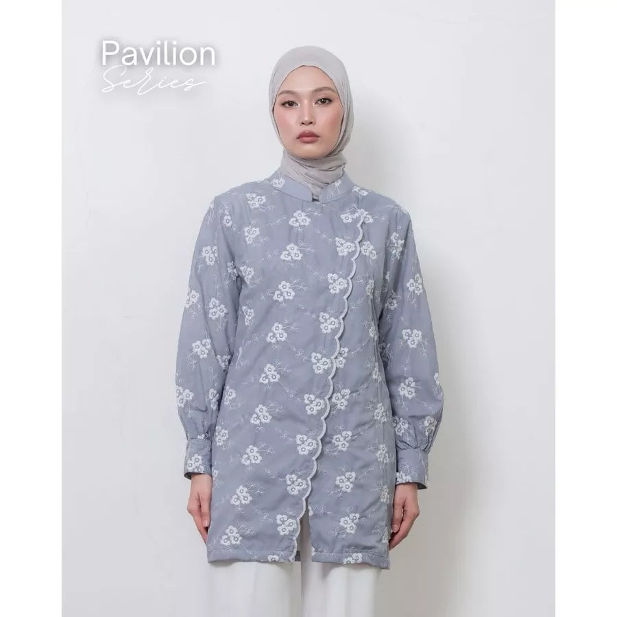 Woman wearing a sky blue floral tunic by Atala Scarves with white pants on a plain background.
Seorang wanita mengenakan tunik bunga berwarna biru langit dari Atala Scarves dengan celana putih di latar belakang polos.