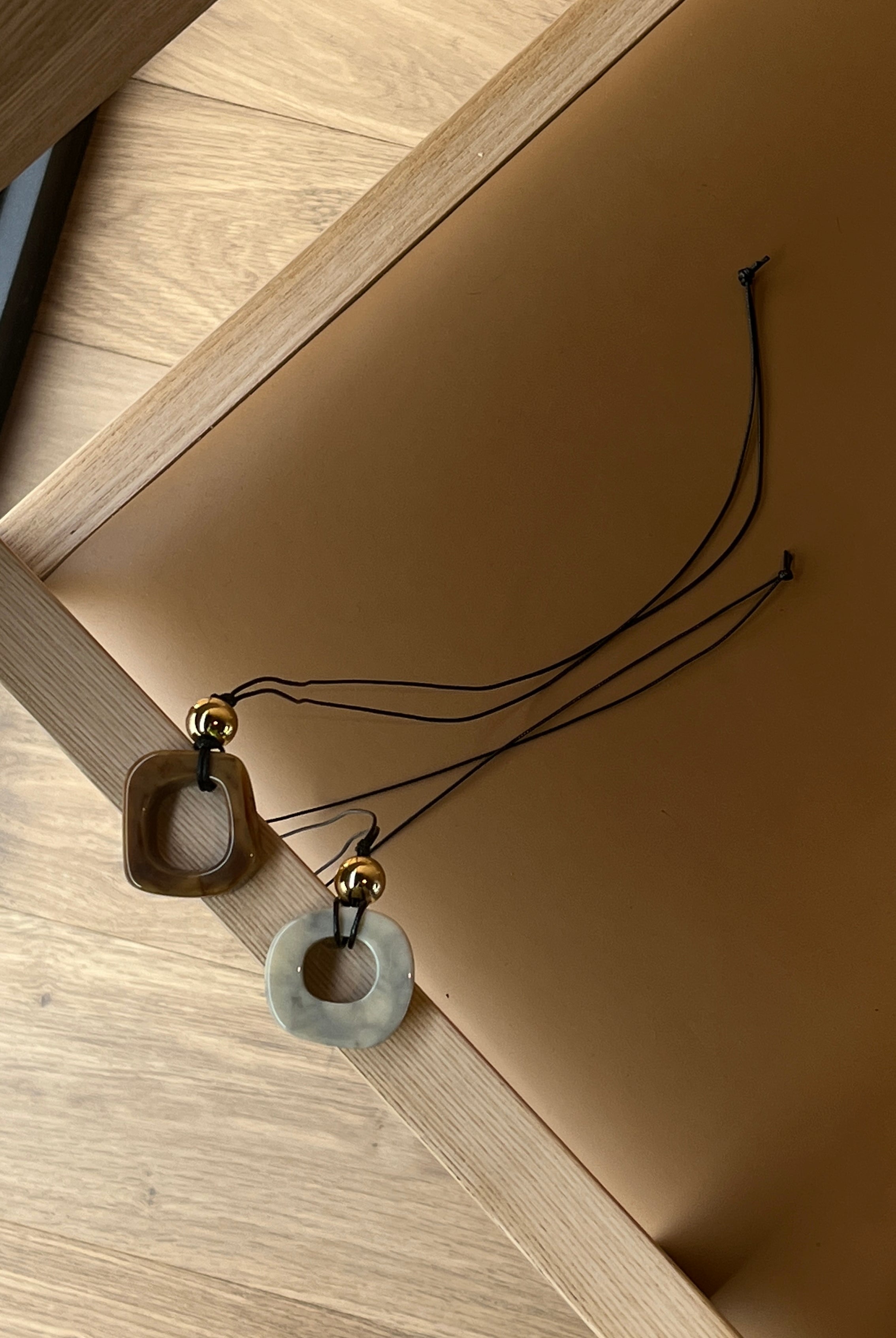Two necklaces with pebble stone pendants by Darje on a wooden surface