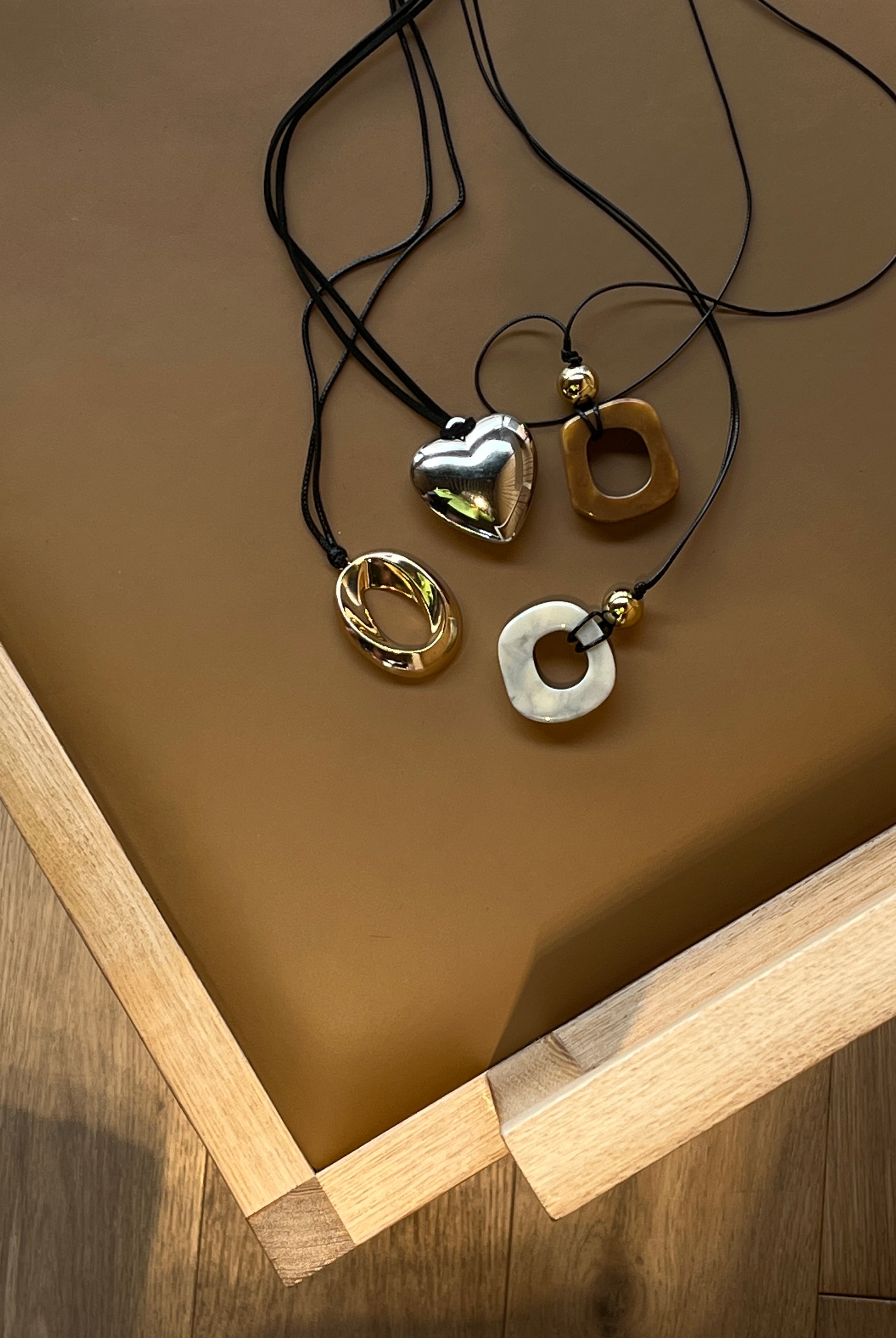 Four necklaces by Darje with different pendants on a brown surface