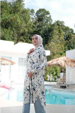 Seorang wanita memakai tunik berwarna putih dengan motif floral biru.