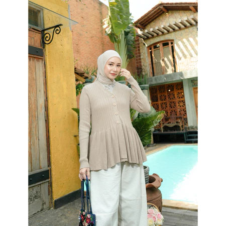 Woman in beige cardigan from Haidee Orlin and white pants standing by a poolside with a building and palm tree in the background.