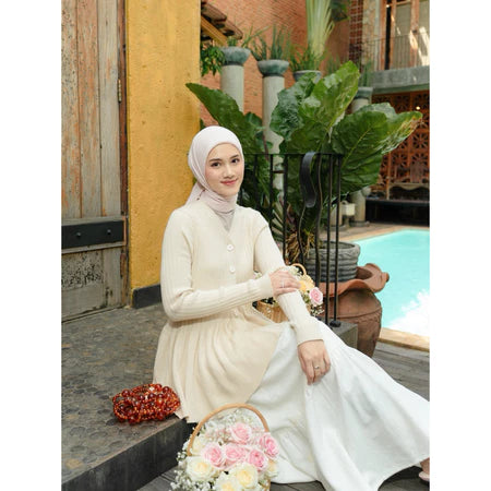 Woman in a cream cardigan from Haidee Orlin sitting outdoors with plants and a pool in the background