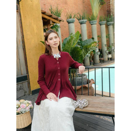 Woman in a red cardigan from Haidee Orlin sitting outdoors with plants and a pool in the background
