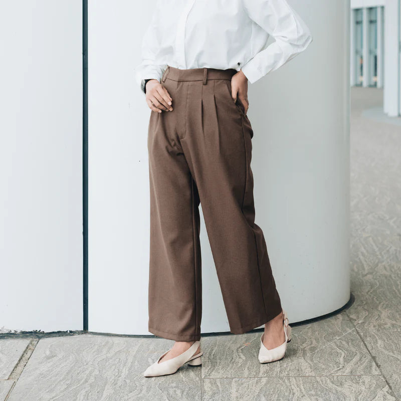 Person wearing a white shirt and dark brown wide-leg pants from Atala Scarves standing against a white wall.