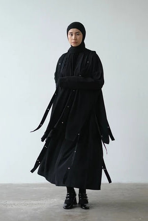 Person wearing a long black coat and skirt by Rashawl against a plain background