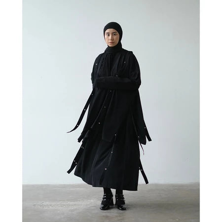 Person wearing a long black coat and skirt by Rashawl against a plain background
